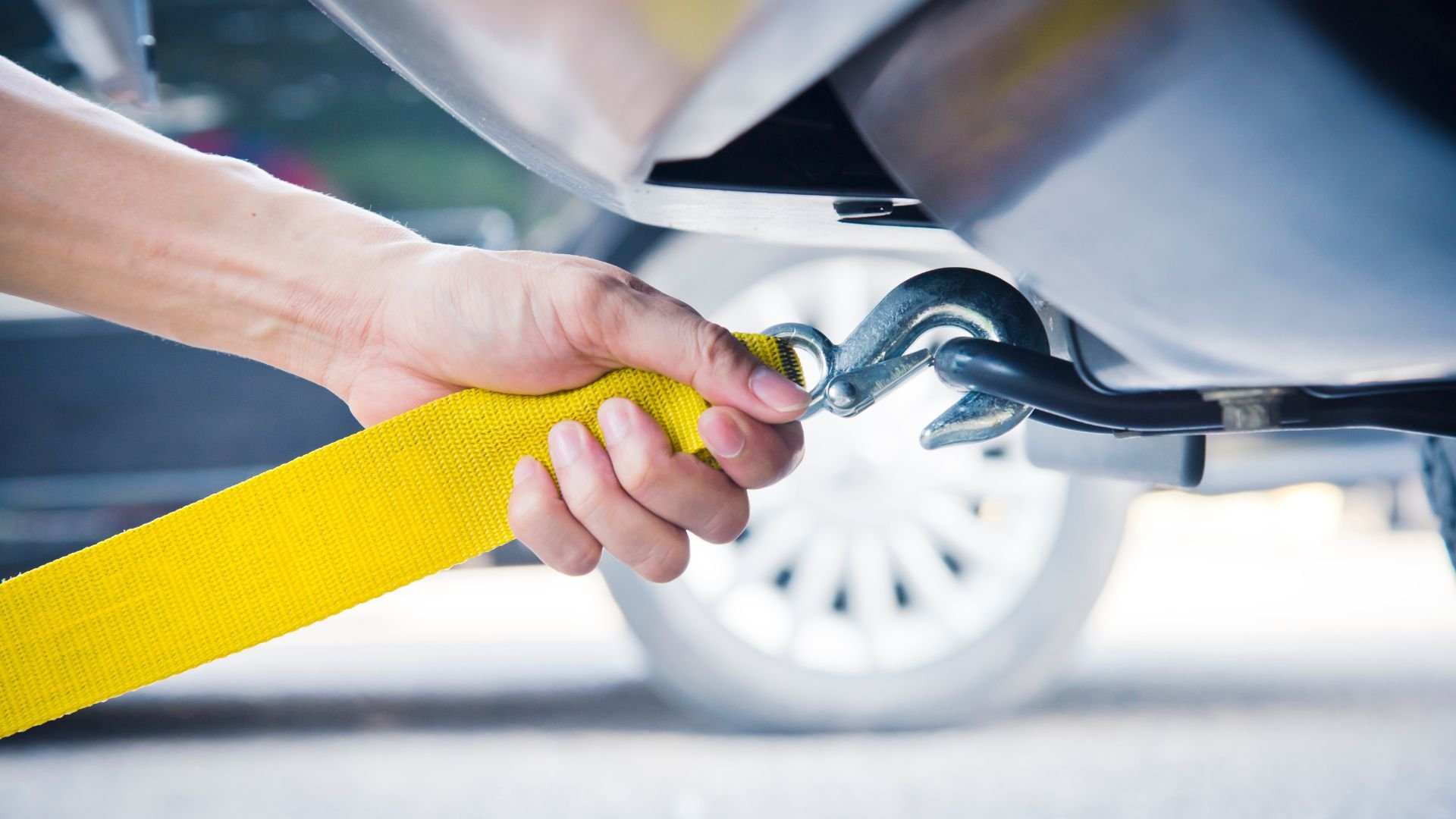 Hand holding yellow tow strap connecting to vehicle hook