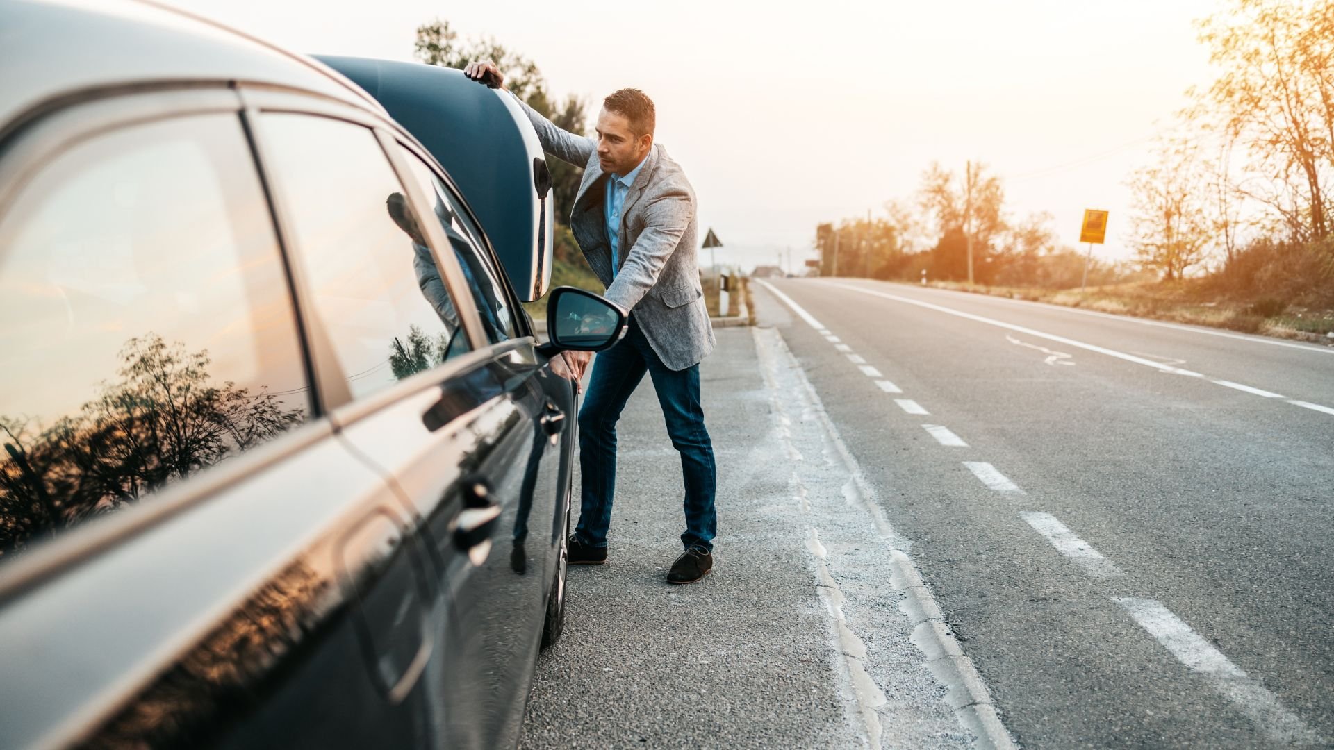 Businessman opening car hood on roadside during sunset