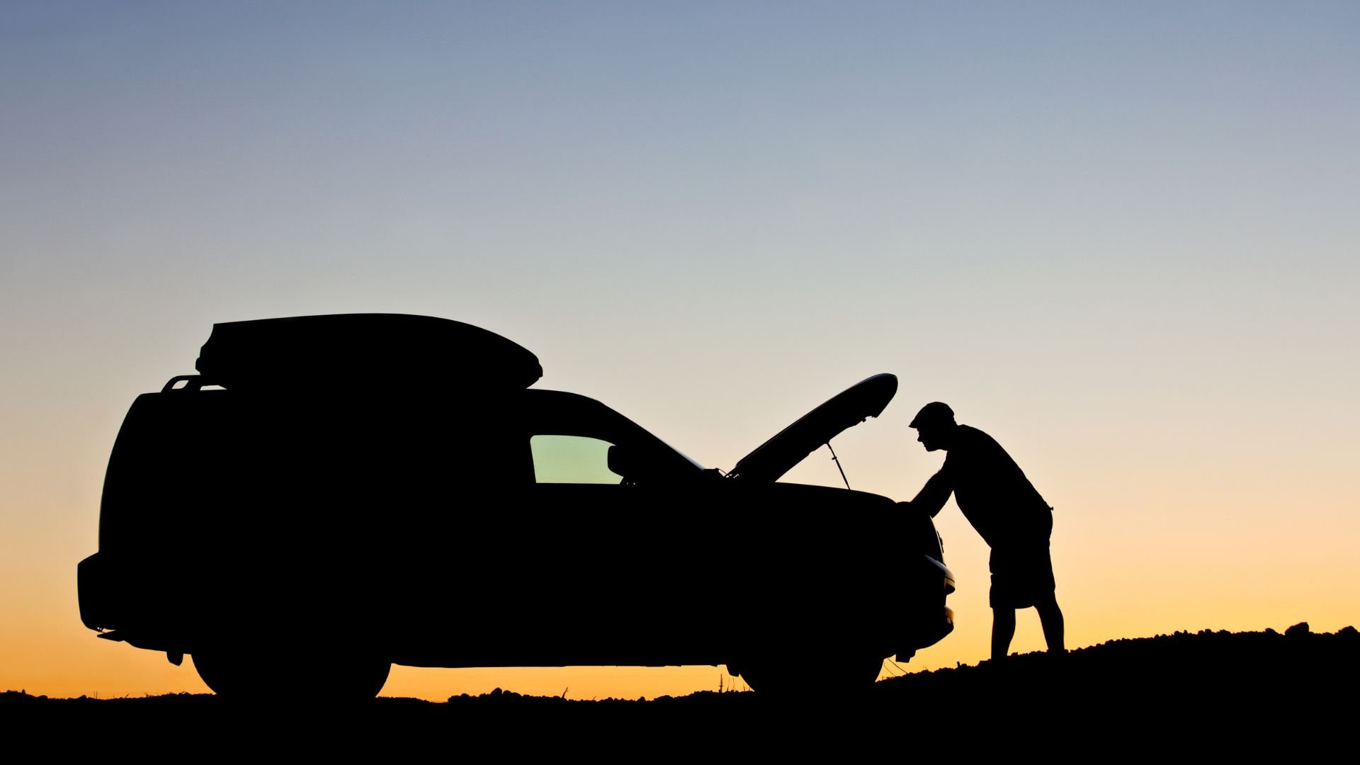 Silhouette of person checking car hood at sunset with roof cargo box