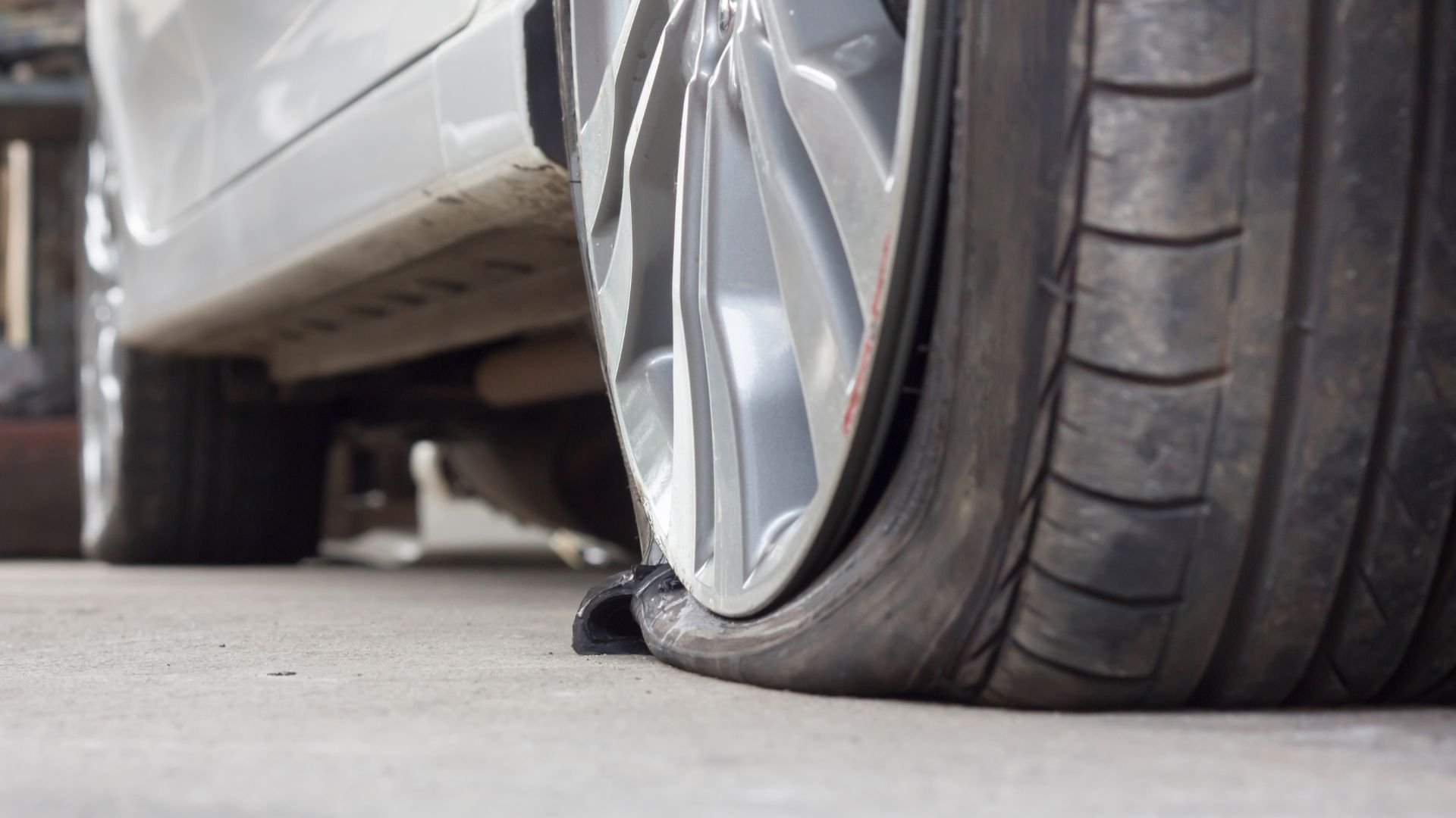 Flat tire on a car, showing deflated rubber against concrete floor