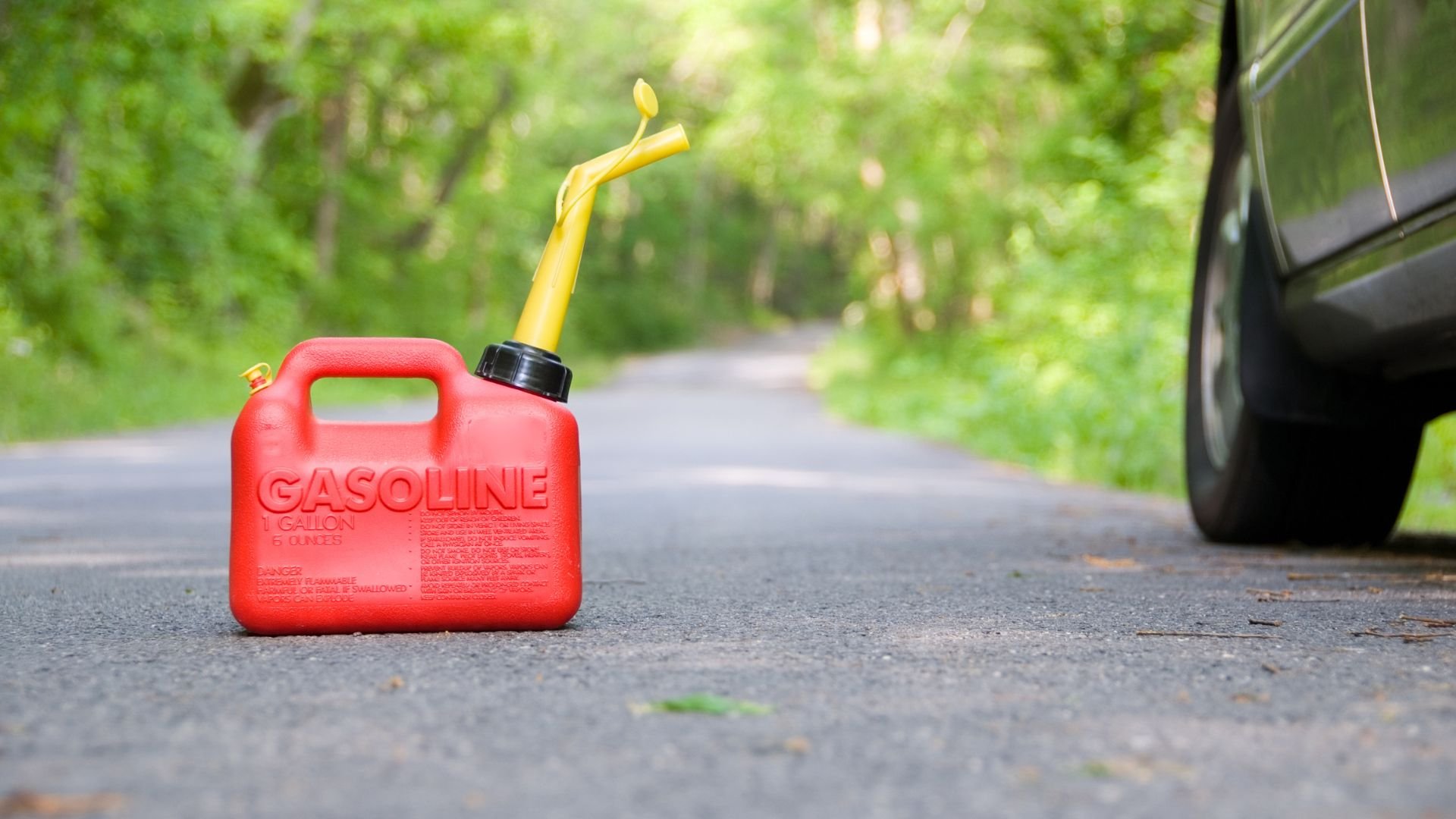 Red gasoline container with yellow spout on road near parked vehicle