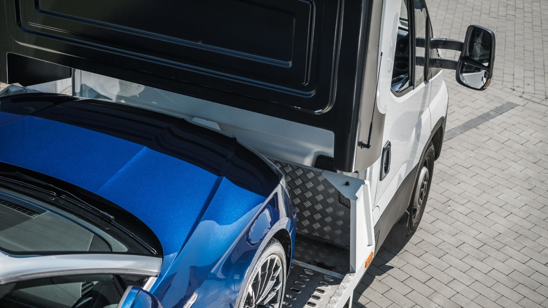 Blue car loaded onto white tow truck on brick pavement