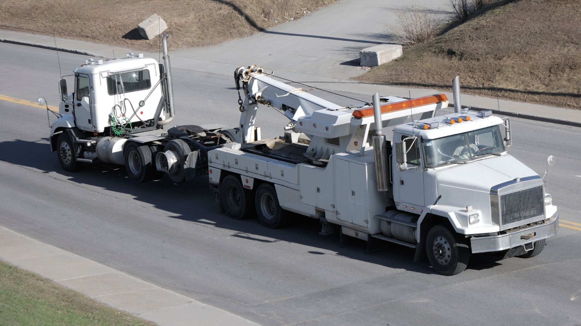 White tow truck pulling another truck on a rural highway