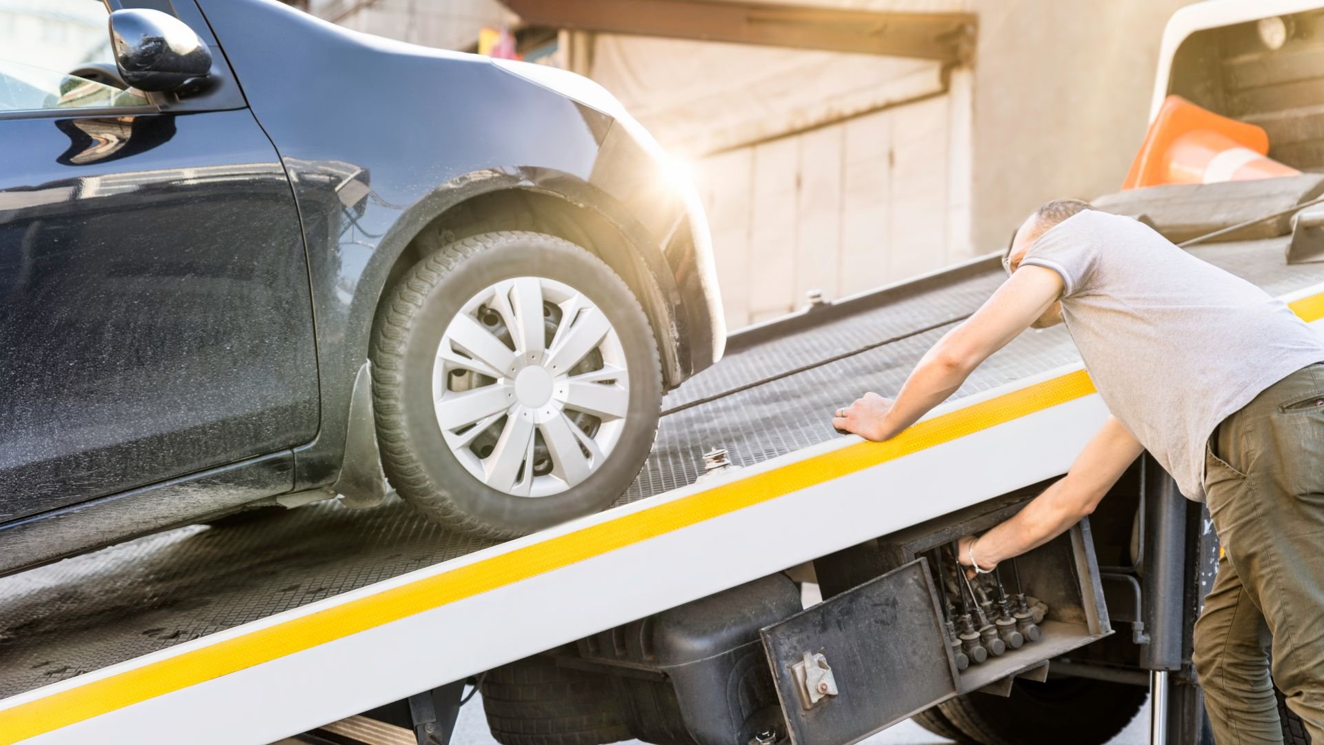 Car being loaded onto a tow truck's flatbed with yellow striped ramp