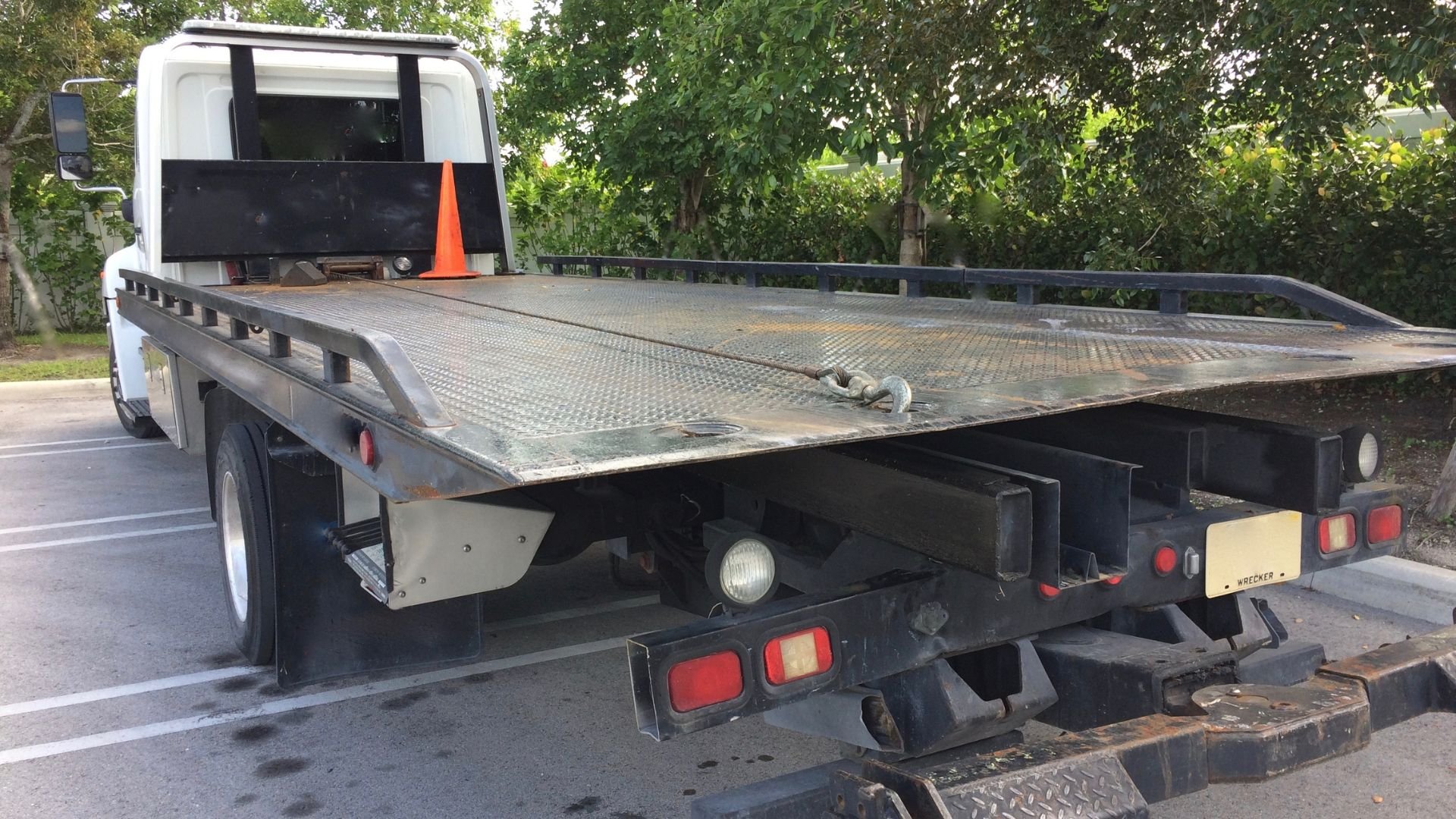 White flatbed tow truck with orange safety cone parked near trees