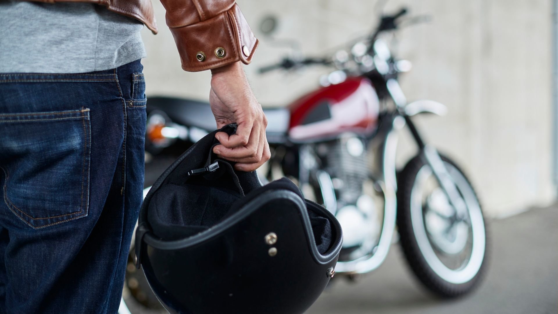 Motorcyclist holding black helmet with vintage motorcycle in background
