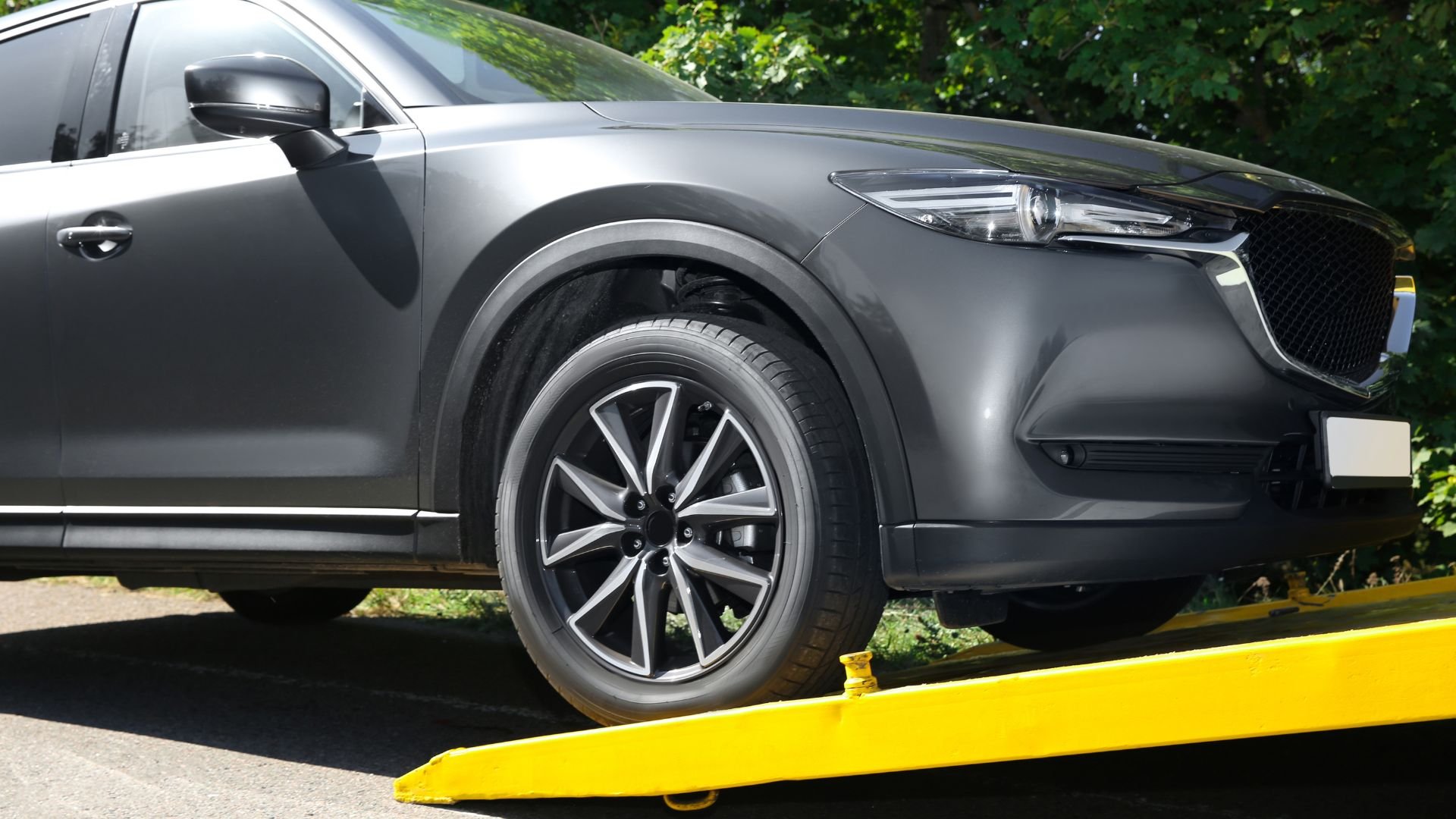 Gray SUV with stylish wheel on yellow platform near green trees