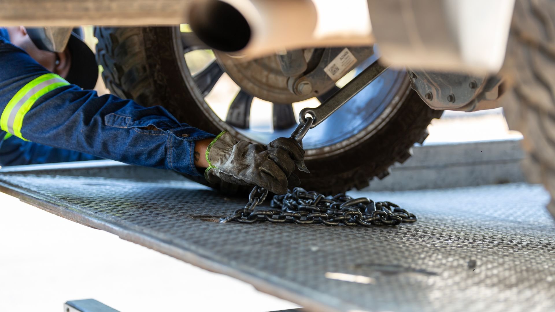 Worker in safety vest secures chain near vehicle tire on metal platform